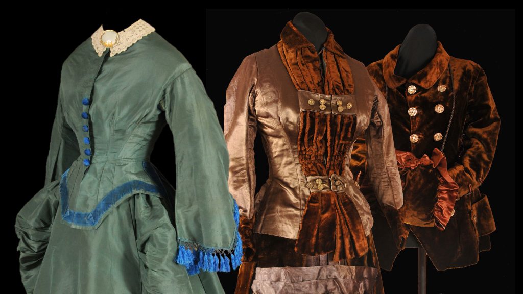 Three headless historical outfits on black: a green embroidered dress, a brown fur-trimmed coat, and a dark ornate jacket with red sash.